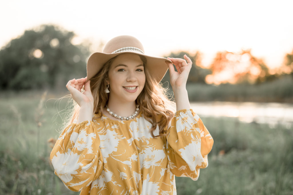 senior photography at sunset in river with hat