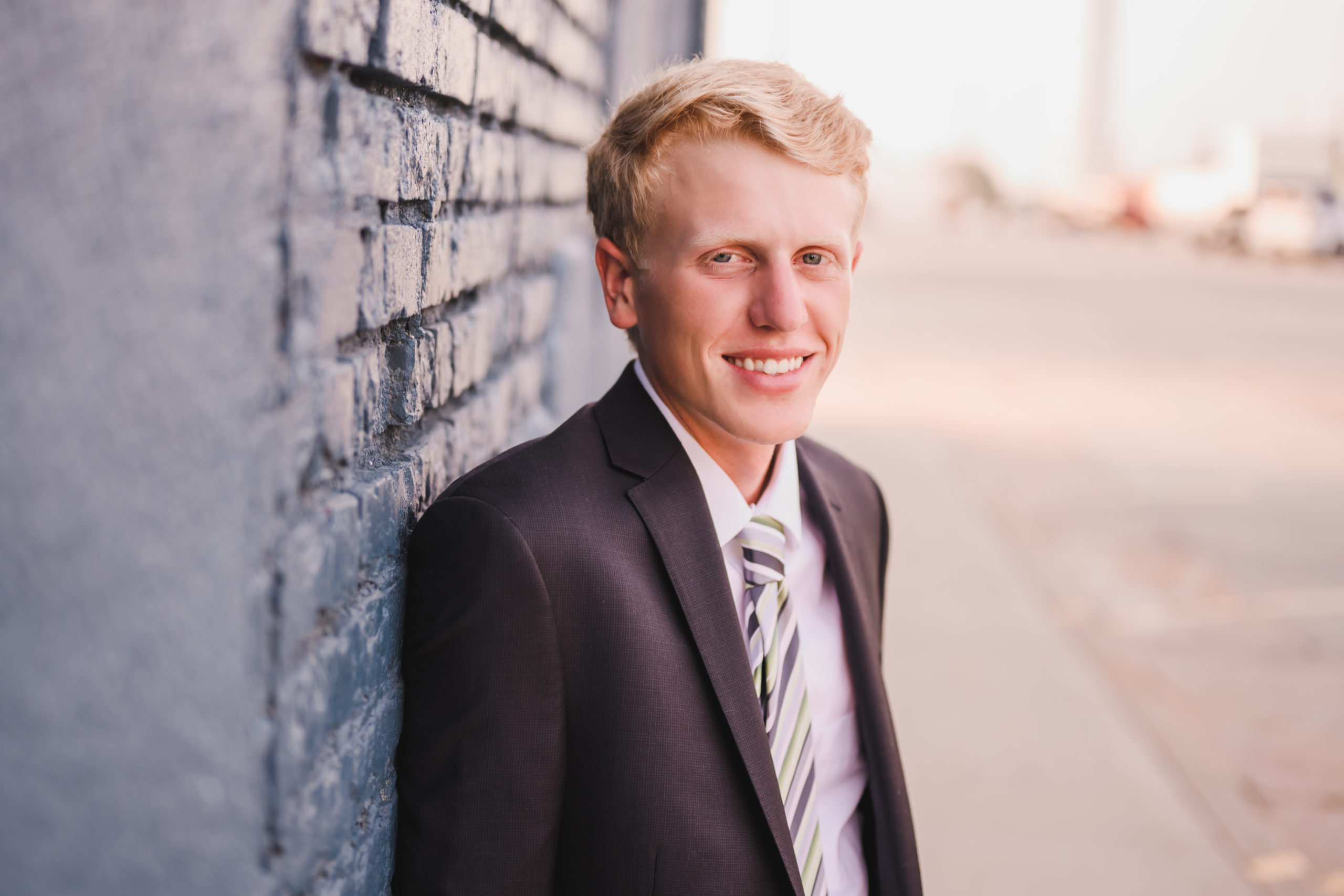 graduation photo of young man in suit and tie leaning against a brick wall